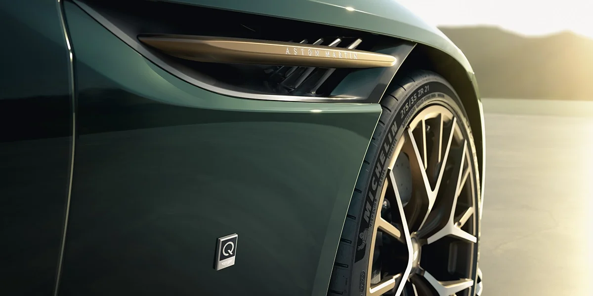 Close-up of Aston Martin Vanquish Volante fender with gold accent and “Q by Aston Martin” badge, highlighting bespoke British design.