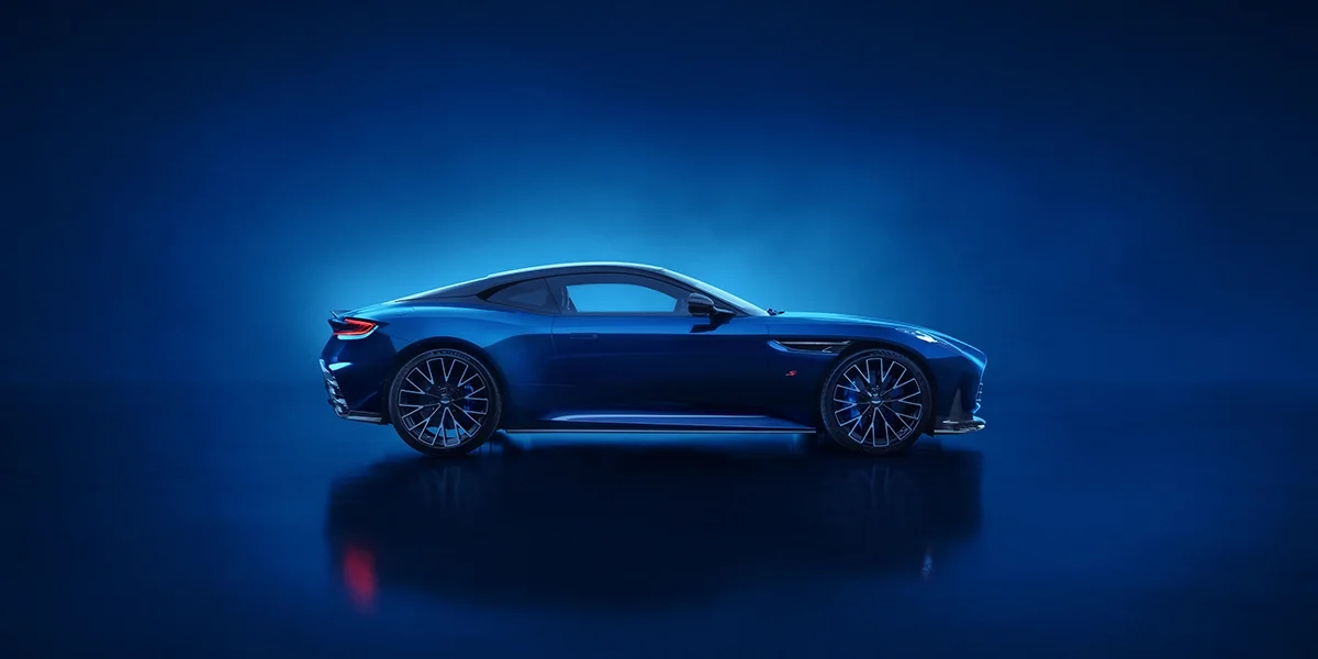 Overhead front three-quarter view of the Aston Martin DB12 S coupe, finished in metallic blue, emphasizing its aerodynamic shape and bold front design.