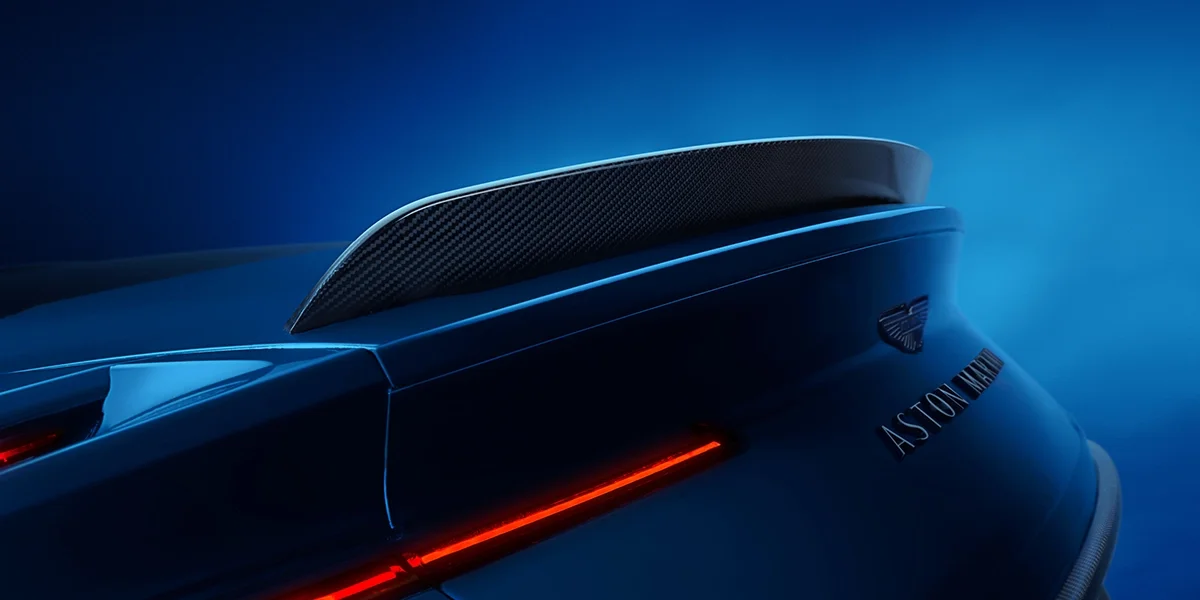 Engine close-up of the Aston Martin DB12 S showing a badge labeled “Hand Built in Great Britain” with the model name and inspector’s signature on a carbon fiber panel.