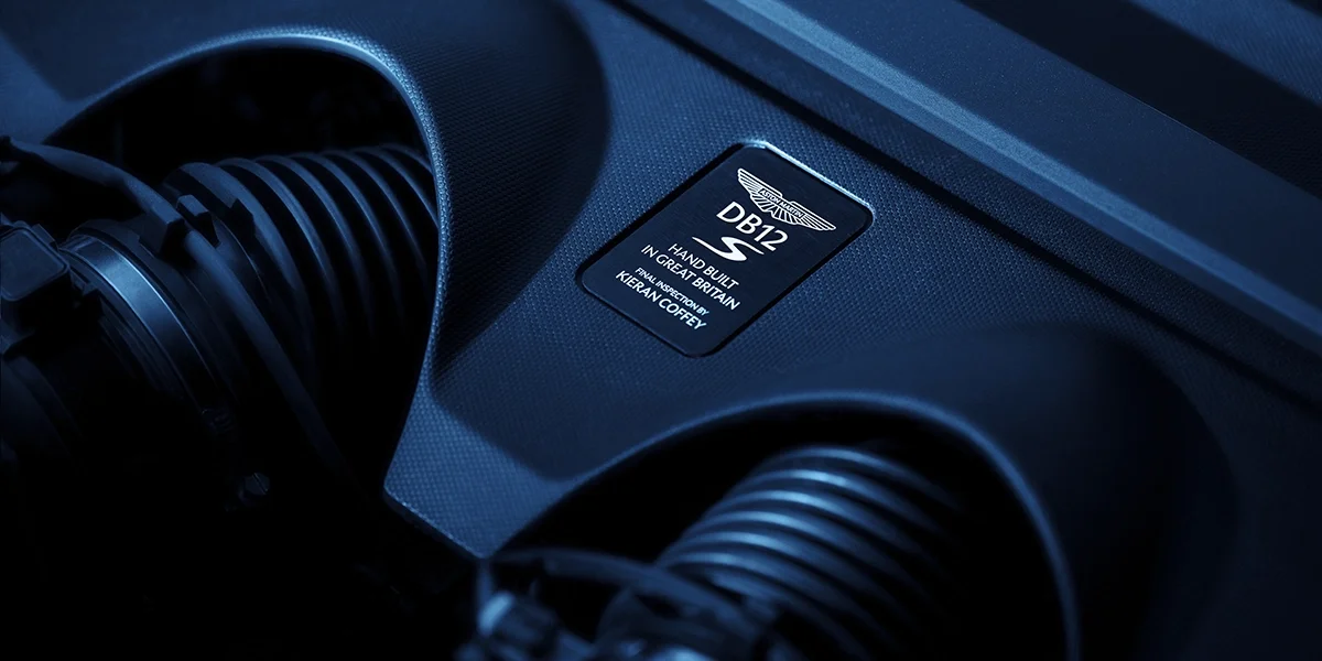 Top-down rear three-quarter view of the Aston Martin DB12 S, emphasizing the black roof, sculpted rear fenders, and integrated taillights.