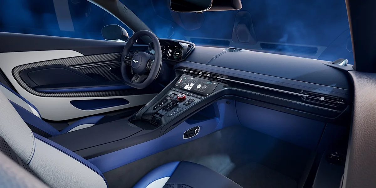 Side profile of the Aston Martin DB12 S in metallic blue, displaying its low-slung coupe proportions, aerodynamic lines, and large alloy wheels.