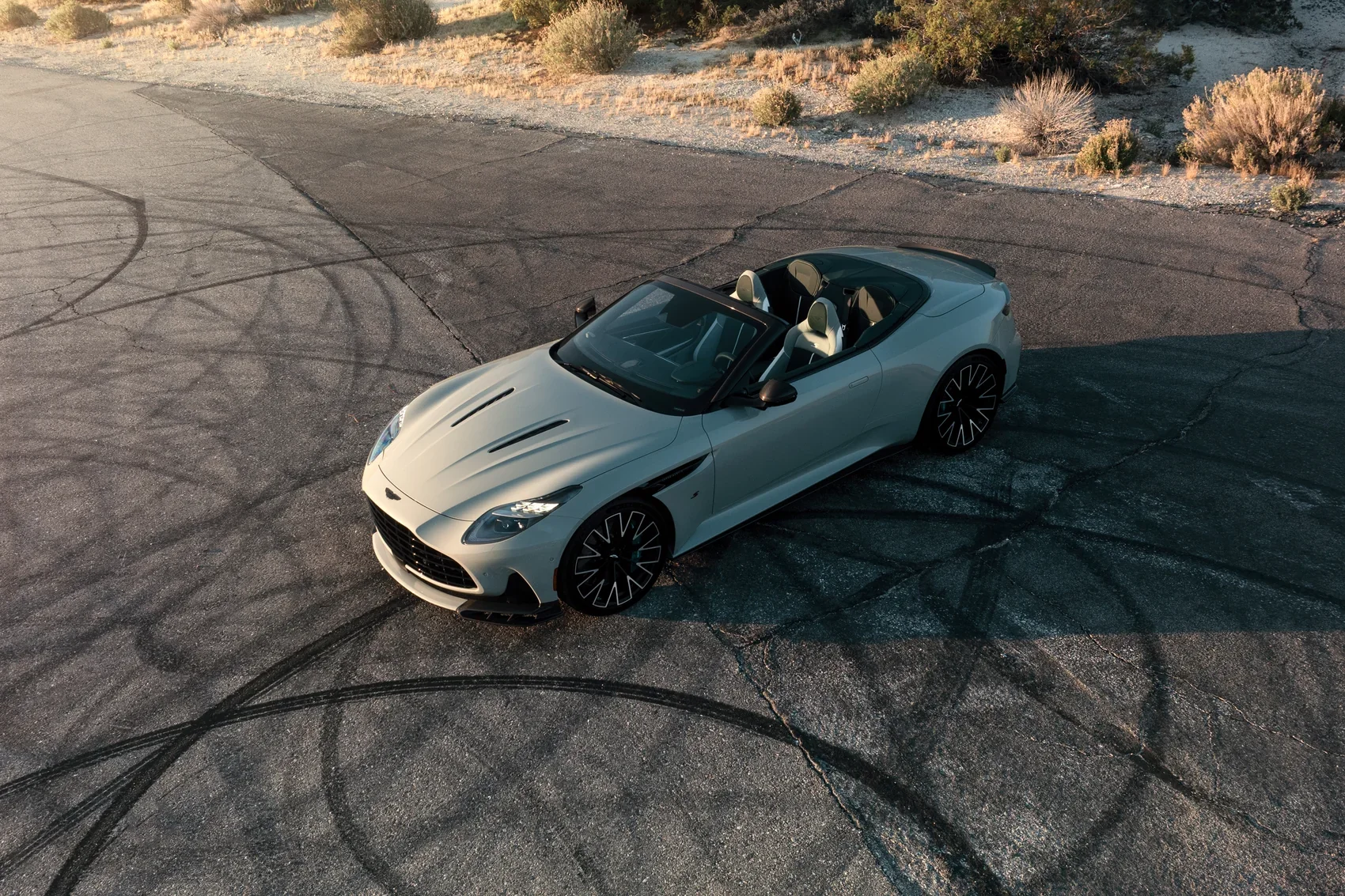 Aerial view of a white Aston Martin DB12 Volante convertible on a desert road at sunset