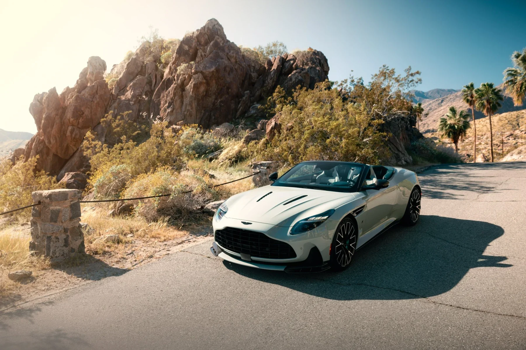 White Aston Martin DB12 Volante convertible parked on a desert road with rocky hills and palm trees